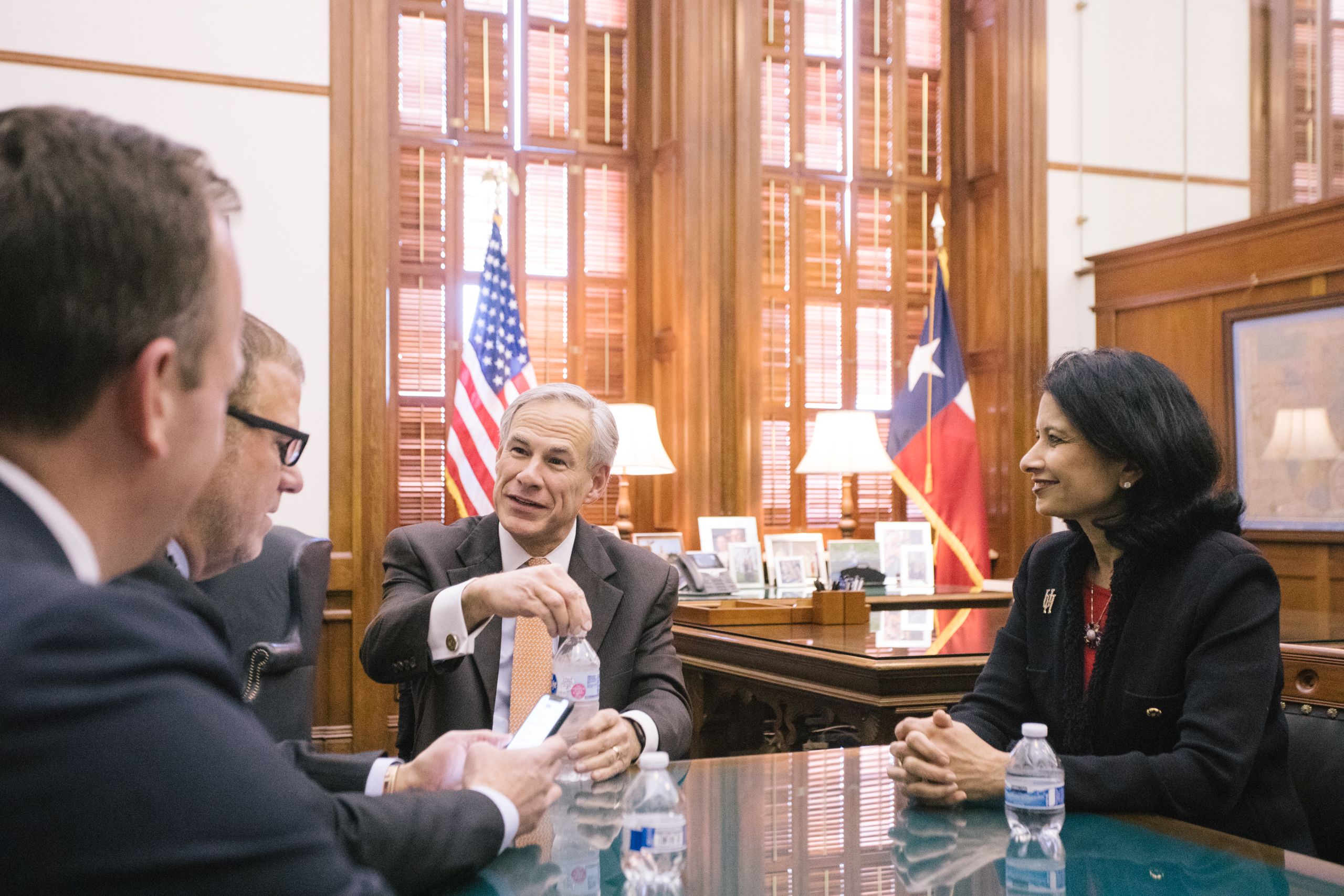 UH President Renu Khator and UHS Chairman Tilman Fertitta sitting at a table with Gov. Greg Abbott.