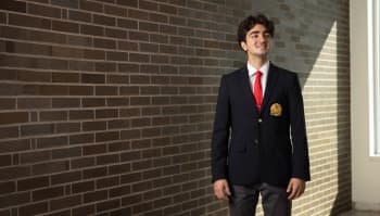 This is a photo of UH Senior Daniel Sadegi. He stands in front of a brick wall and is smiling.